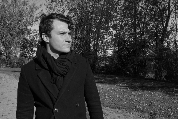 joseph-alai-black-and-white-portrait A black and white portrait of Joseph Alai standing outdoors on a path, looking thoughtfully to the side.